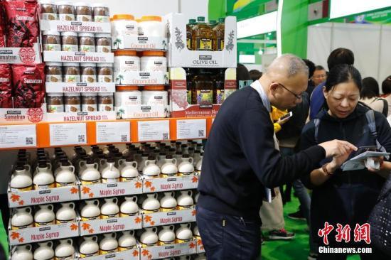 资料图:首届中国国际进口博览会食品及农产品展区,参观者与商家交流商品信息。中新社记者 殷立勤 摄
