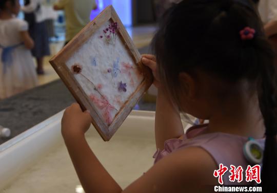 图为小朋友欣赏自己制作的古法花草纸。 周毅 摄